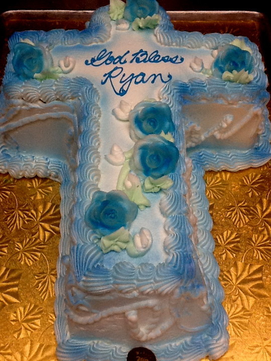 Blue cake with icing flowers in the shape of a cross with text that read God Bless Ryan