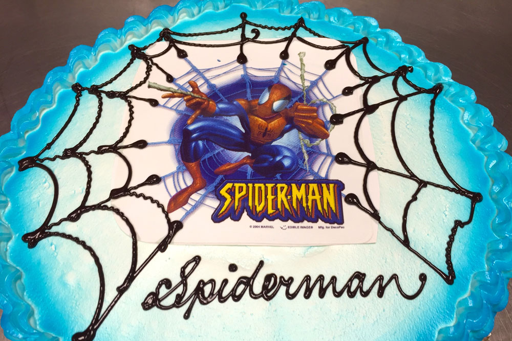 Decorated cake with blue icing, piped spiderwebs and Spider-Man decal